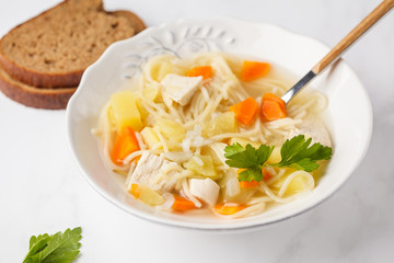 Chicken soup with noodles and vegetables in a white plate.