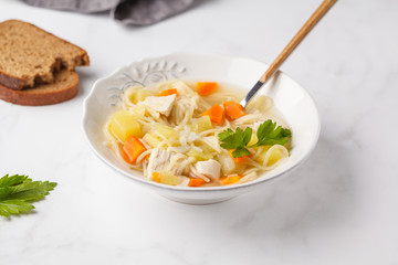 Chicken soup with noodles and vegetables in a white plate.