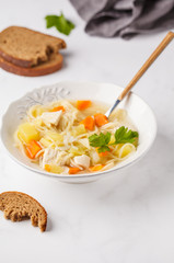 Chicken soup with noodles and vegetables in a white plate.