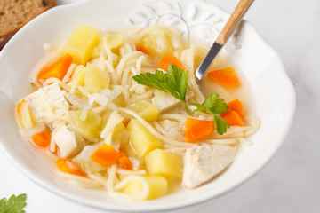 Chicken soup with noodles and vegetables in a white plate.
