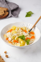 Chicken soup with noodles and vegetables in a white plate.