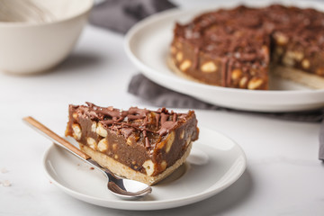 Piece of raw vegan chocolate cake with nuts and chocolate in white plate. Healthy vegan food concept.