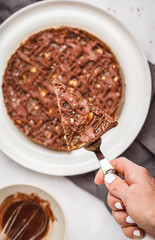 Piece of raw vegan chocolate cake with nuts and chocolate in white plate. Healthy vegan food concept.