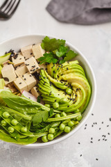 Green buddha bowl with tofu, rice, avocado and vegetables. Healthy vegan food concept.