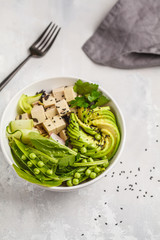 Green buddha bowl with tofu, rice, avocado and vegetables. Healthy vegan food concept.
