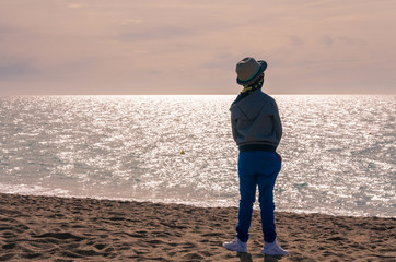 A young boy stands on a beach and looks out to sea.