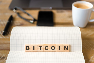 Closeup on notebook over vintage desk background, front focus on wooden blocks with letters making Bitcoin text