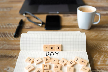 Closeup on notebook over vintage desk background, front focus on wooden blocks with letters making Tax Day text