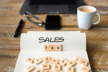 Closeup on notebook over vintage desk background, front focus on wooden blocks with letters making Sales Tax text