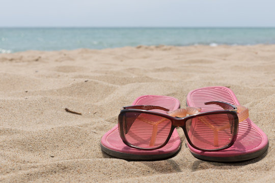 sunglasses and pink flip flops on the beach against the sea