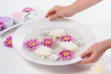Fototapeta na wymiar cropped shot of woman holding bath for nails with flowers and aroma candles at table in beauty salon