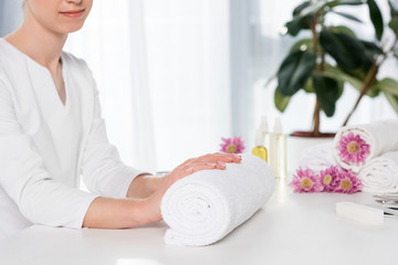 woman holding hands with manicure at table with towels, flowers, aroma oil bottles in beauty salon