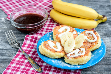 Cottage cheese pancakes on blue plate on a wooden table with sour cream, jam and banana closeup.
