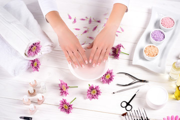 Obraz na płótnie Canvas cropped image of woman receiving bath for nails at table with flowers, towels, colorful sea salt, aroma oil bottles, nail polishes, cream container and tools for manicure in beauty salon