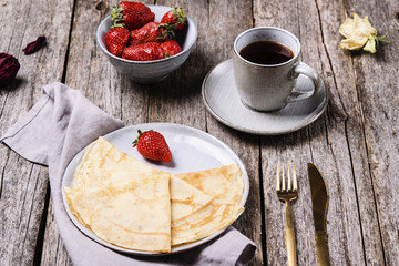 Openwork thin cheese crepes served with strawberry on wooden background. Homemade pancakes. Delicious breakfast