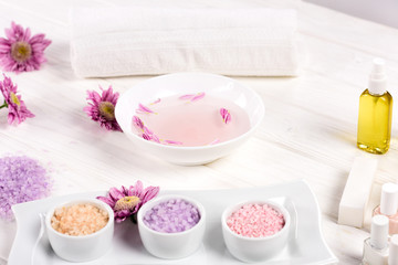close up shot of bath for nails with petals at table with flowers, towel, colorful sea salt, nail polishes and aroma oil bottle for manicure and pedicure in beauty salon