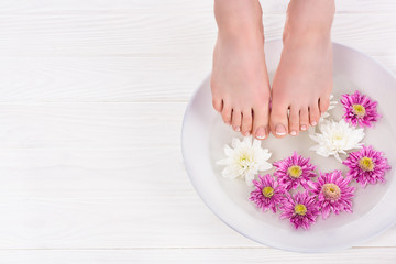 partial view of barefoot woman receiving bath for nails flowers in beauty salon