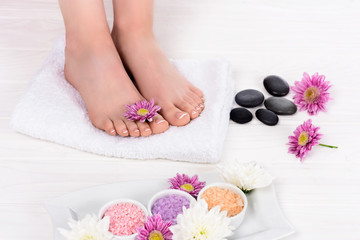 Obraz na płótnie Canvas cropped image of barefoot woman on spa treatment with towel, flowers, colorful sea salt and spa stones