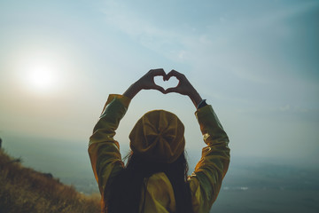 A young girl making heart symbol with her hands at sunset - 208747778