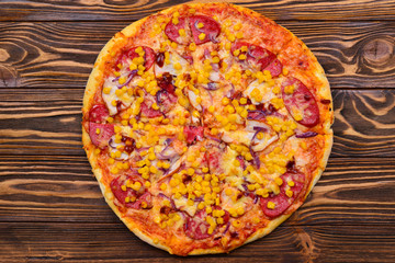 Pizza with salami, tomatoes, corn, chicken on wooden table.