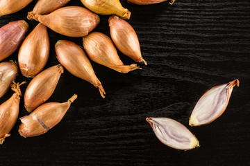 Long golden shallots one cut in two halves flatlay isolated on black wood background.