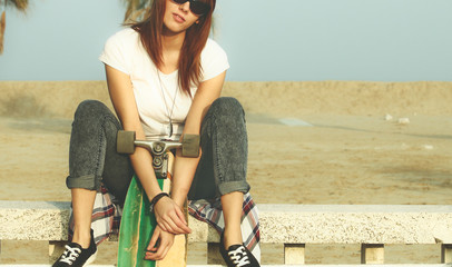 young skater girl sitting on bench holding a  skateboard. midsection crop focused on hands and skate board.