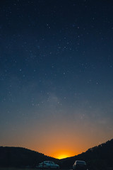 Fototapeta premium a beautiful view of the starry sky, and mountains, the sky full of stars, great panorama, in the foreground cars and a trailer for a boat, vertical photo