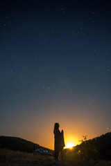 Naklejka na ściany i meble alone woman silhouette in mountains, girl wrapped up in a plaid looks at the sky, enjoying view of amazing night sky full of stars, vertical photo