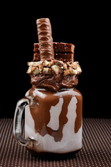 Chocolate extreme milkshake with brownie cake, chocolate paste and sweets. Crazy freakshake food trend.