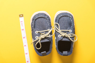baby shoes with measuring tape on yellow background