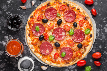 Italian pizza on thin dough with tomato sauce, salami, cheese, olives and Basil