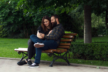 Obraz premium Happy young couple sitting in a park bench and using a smart phone