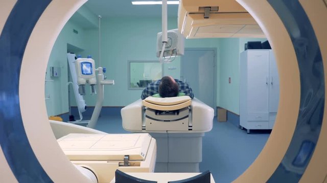 Man lays in Magnetic Resonance Image device. Male patient is lying in a hospital room with working CAT-scanner