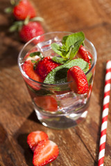 Summer cold drink with strawberries, mint and ice in glass on wooden background. Closeup of cocktails with fresh fruits.