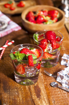 Summer cold drink with strawberries, mint and ice in glass on wooden background. Closeup of cocktails with fresh fruits.