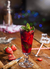 Summer cold drink with strawberries, mint and ice on wooden bar counter . Closeup of cocktail with fresh fruits.