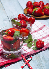 Summer cold drink with strawberries, mint and ice in glass on blue background. Closeup of cocktails with fresh fruits.