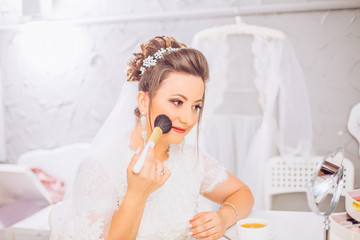 Obraz na płótnie Canvas Attractive young bride preparing for wedding in the morning, drinking coffee with smatphone smiling and looking to the mirror. Bride waiting for the groom. Wedding concept.