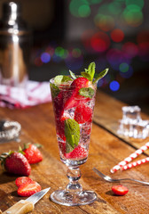 Summer cold drink with strawberries, mint and ice on wooden bar counter . Closeup of cocktail with fresh fruits.