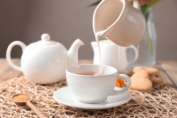 Pouring milk into cup with aromatic tea on wicker mat