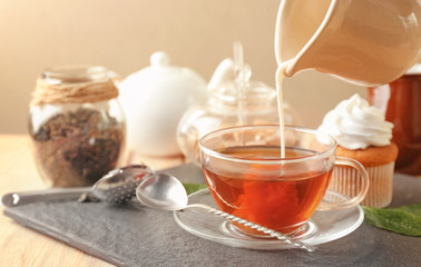 Pouring milk into cup with aromatic tea on slate plate