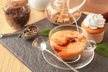 Pouring milk into cup with aromatic tea on slate plate