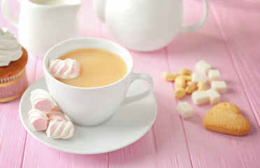 Cup of aromatic tea with milk and marshmallows on wooden table
