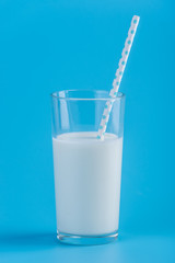 Glass of fresh milk with straw on a blue background. Concept of healthy dairy products with calcium