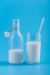 Bottle of fresh milk and a glass with a straw on a blue background. Concept of healthy dairy products with calcium