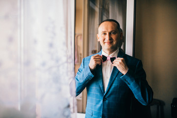 Groom morning preparation, handsome groom getting dressed and preparing for the wedding, the groom wears a jacket and correct bowtie.