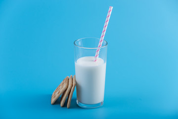 Glass of fresh milk with a straw and cookies on a blue background. Concept of healthy dairy products with calcium