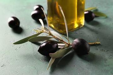 Black olives, green leaves and bottle of oil on color background
