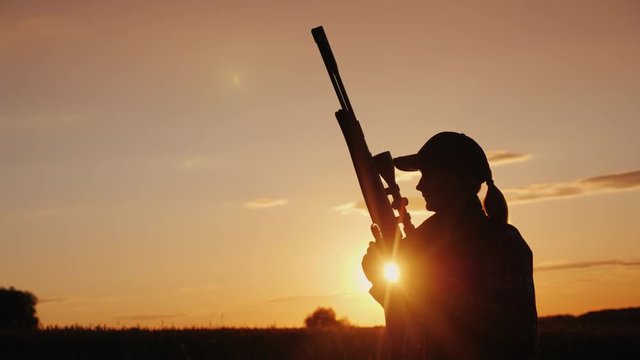 Beautiful silhouette of a woman with a rifle in the rays of the setting sun. Sports shooting and hunting concept