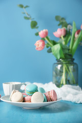 Plate with tasty macarons on table against color background